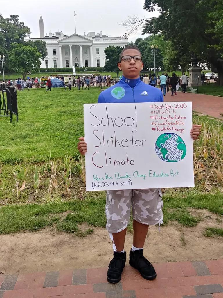 With the White House in the background, a young man holds a poster that reads "School Strike for Climate" 