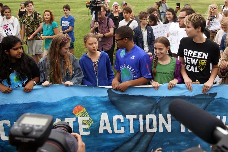 A group of young protesters stands behind a banner that reads in part "Climate Action"
