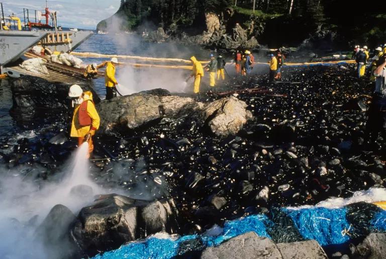 Workers in yellow protective suits and masks hose down oil-covered rocks on a beach