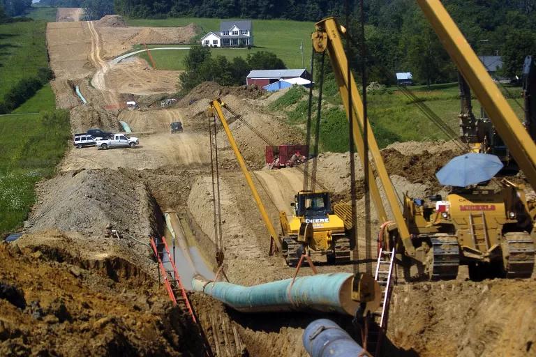 A crane lowers a large section of pipeline into a trench