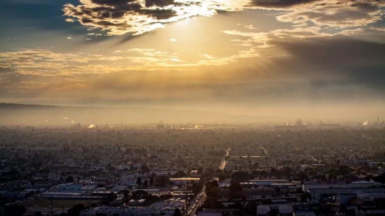 Sunlight breaks through clouds into smoggy air hanging over a neighborhood with an oil refinery in Long Beach, California.