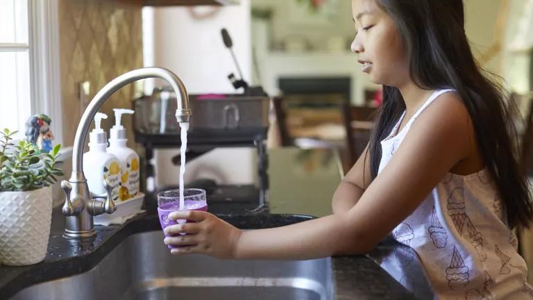 A young girl fills a cup with water from the kitchen sink