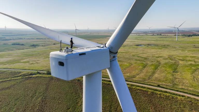 An aerial view of two workers standing on the top of a wind turbine
