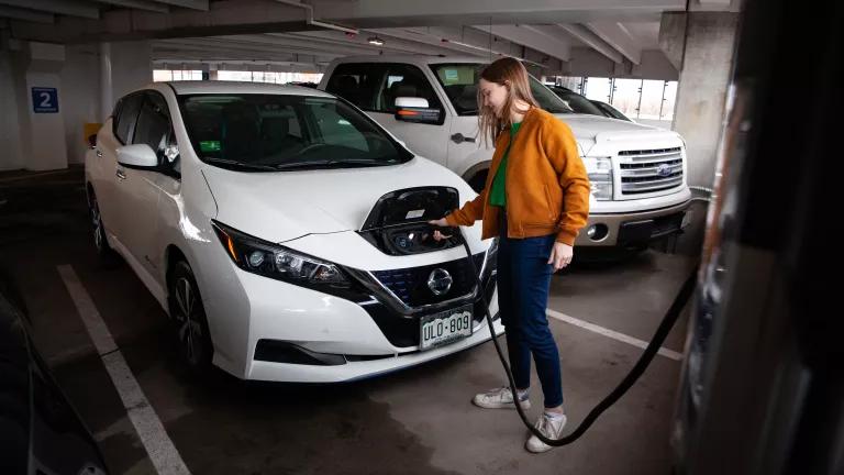 A woman plugging in her electric car at a public parking garage charging station in Fort Collins, Colorado.