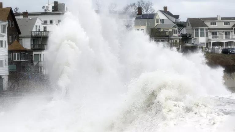 A large wave crashes ashore onto a row of homes