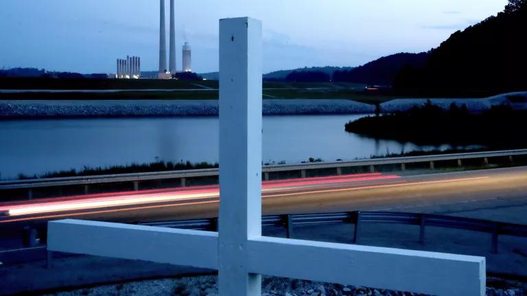 A white cross stands next to a highway with a power plant in the background