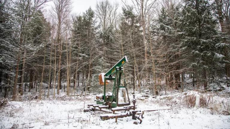 A small oil well sits in snow-covered clearing in a wooded area