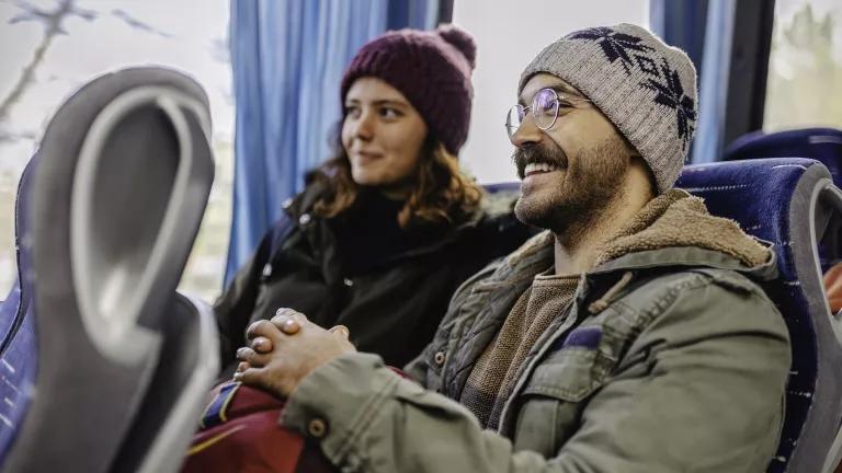 A man and woman in winter clothing sit on a passenger bus