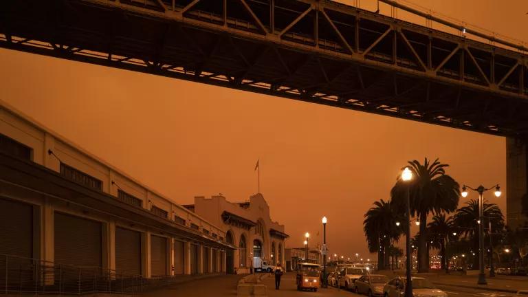 Buildings, trees, and sky turned dark orange by wildfire smoke