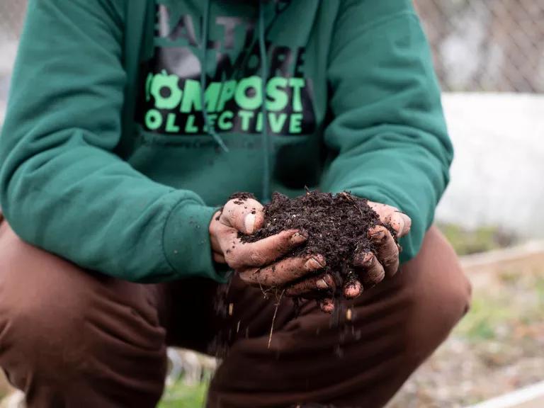 A person holds a large handful of dark brown compost