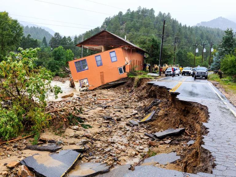 A collapsed house sits next to a paved road that has washed away