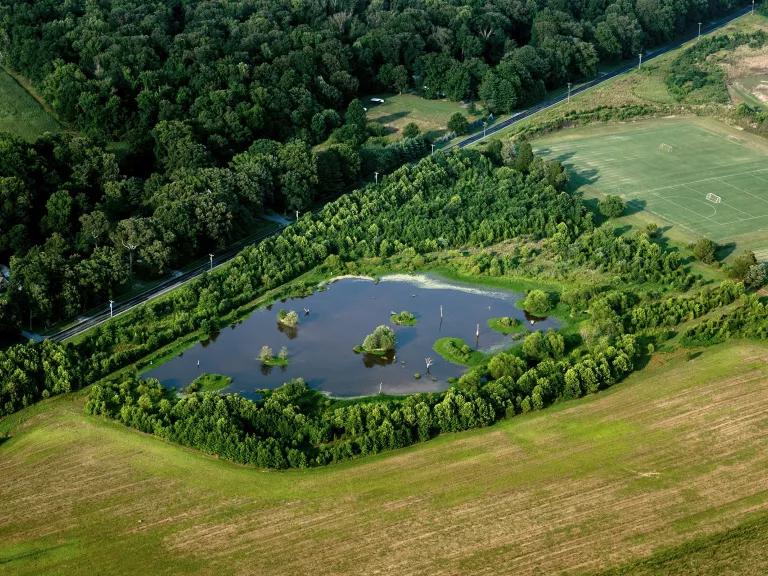 An aerial view of a small pond surrounded by trees and farmland