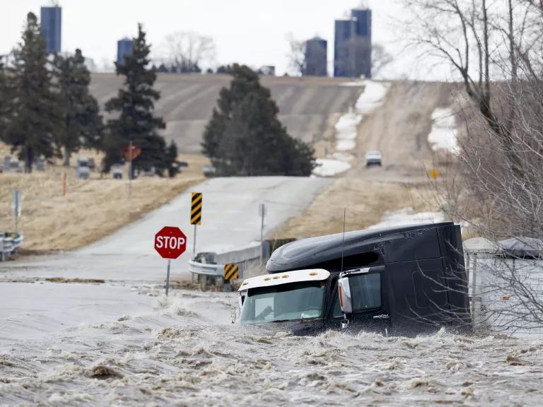 The cab of a truck is submerged in floodwaters next to a rural roadway