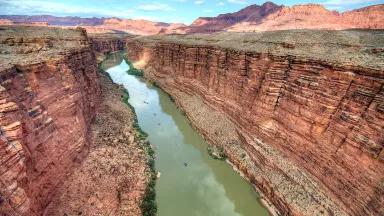 The murky waters of the Colorado River cut through the red landscape at Marble Canyon under a blue sky
