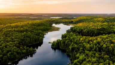 Aerial image of a river running through a verdant boreal forest at sunset