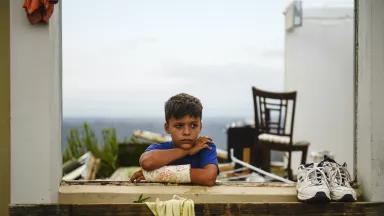 Jake Rios Torres, 9, watches as emergency supplies of food and water are delivered to his family in the mountains above Utuado, Puerto Rico, on October 12, 2017.

The family are sharing a single room after Hurricane Maria destroyed the rest of their home.
