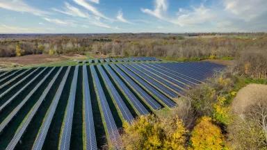 An aerial view of solar panel arrays on a farm in Ohio on a bright, sunny morning in autumn with colorful trees surrounding the area