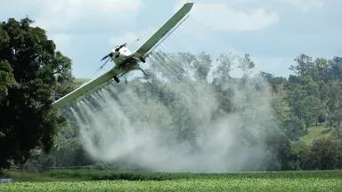 A small crop duster plane spraying pesticide on a field just west of the Border Ranges World Heritage National Park in Australia.