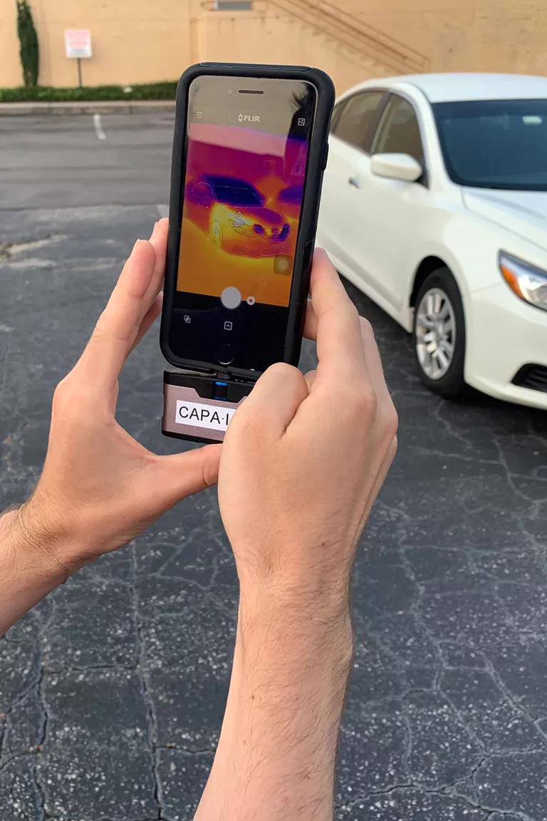 An adult uses a smartphone that has been equipped with a thermal camera attachment.