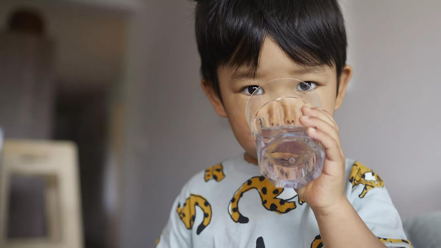 A two-year-old child facing the camera and drinking water from a glass in his home in Brooklyn