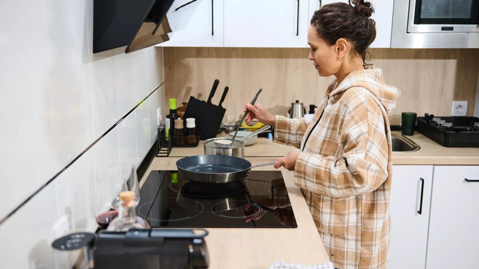 A young woman cooking in her kitchen using an induction stove.