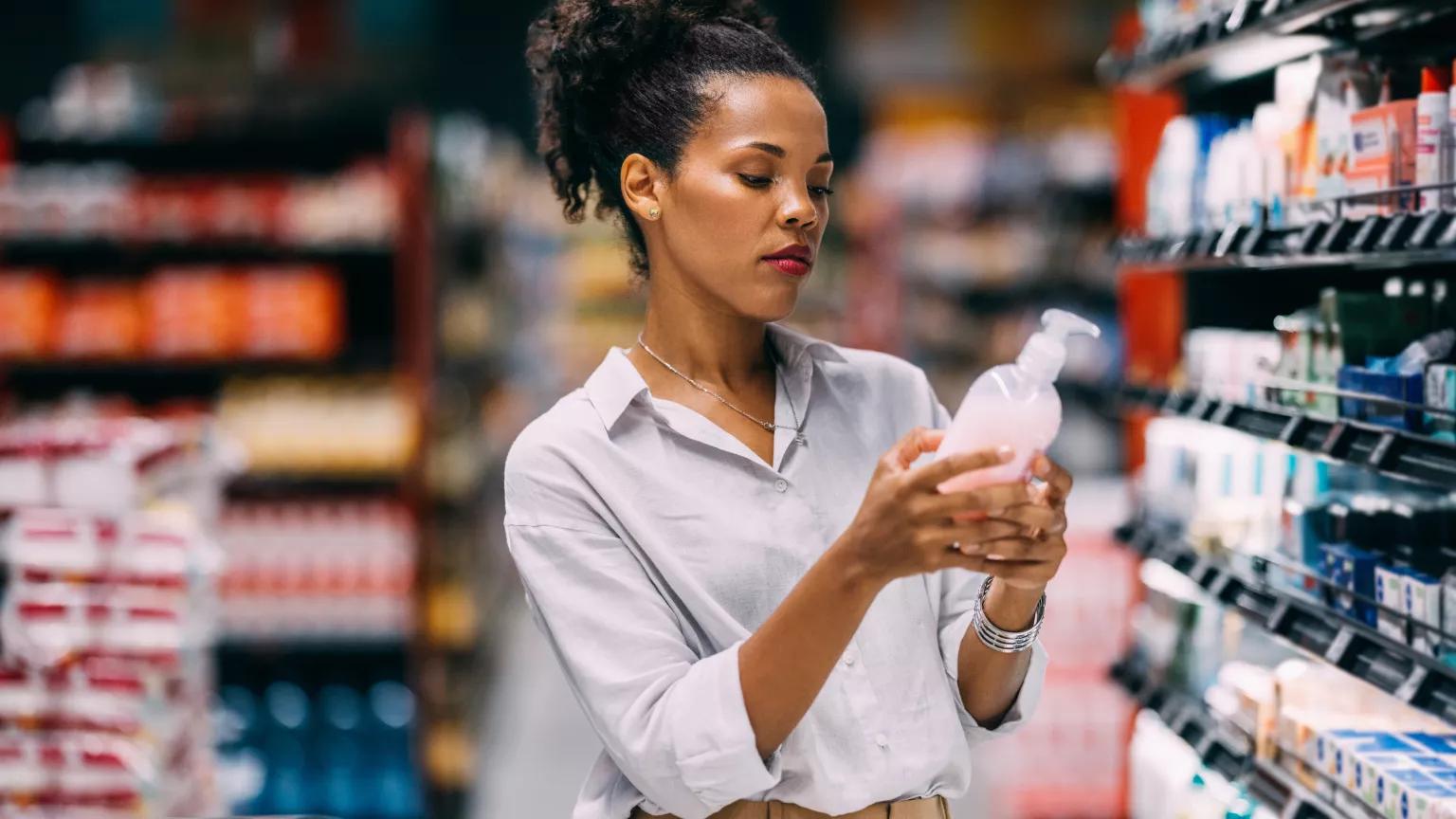 A woman at a grocery store reads ingredients on a soap label.