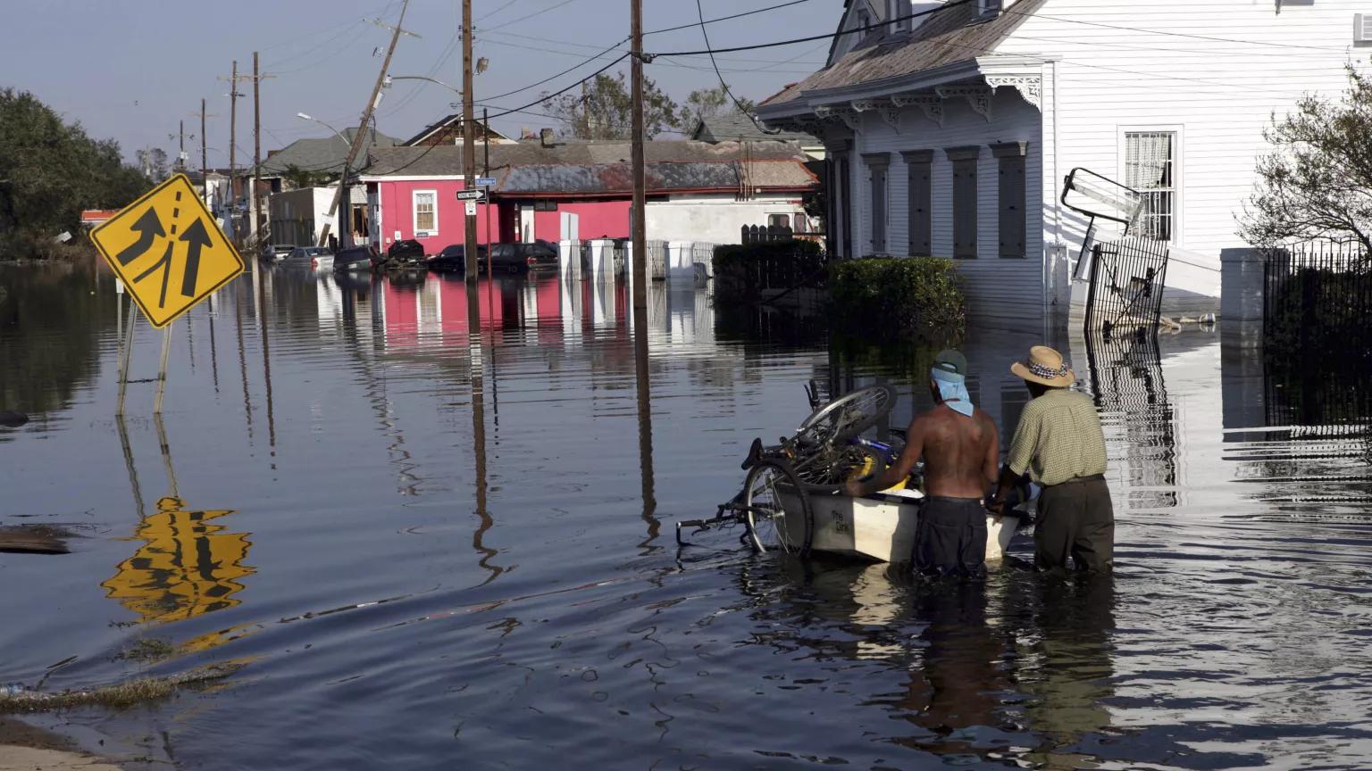 Two men wade through floodwaters as they push a boat filled with bicycles along a residential street in New Orleans, Louisiana, following Hurricane Katrina.