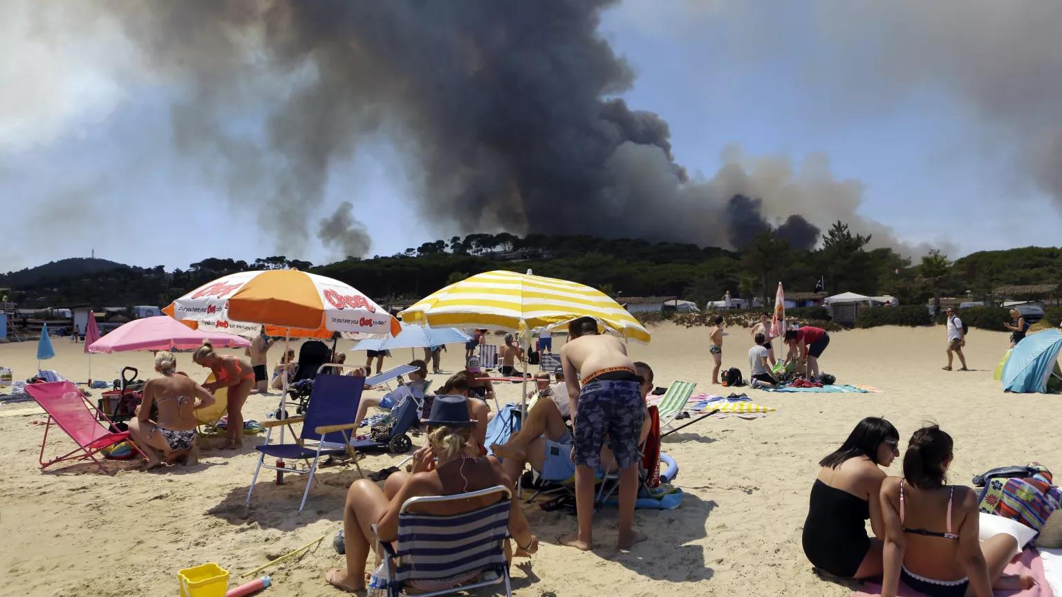 People sunbathing on the beach in Lavandou, French Riviera, as plumes of smoke rise in the air from burning wildfires in the forest of La Londe-les-Maures, France on Wednesday, July 26, 2017.