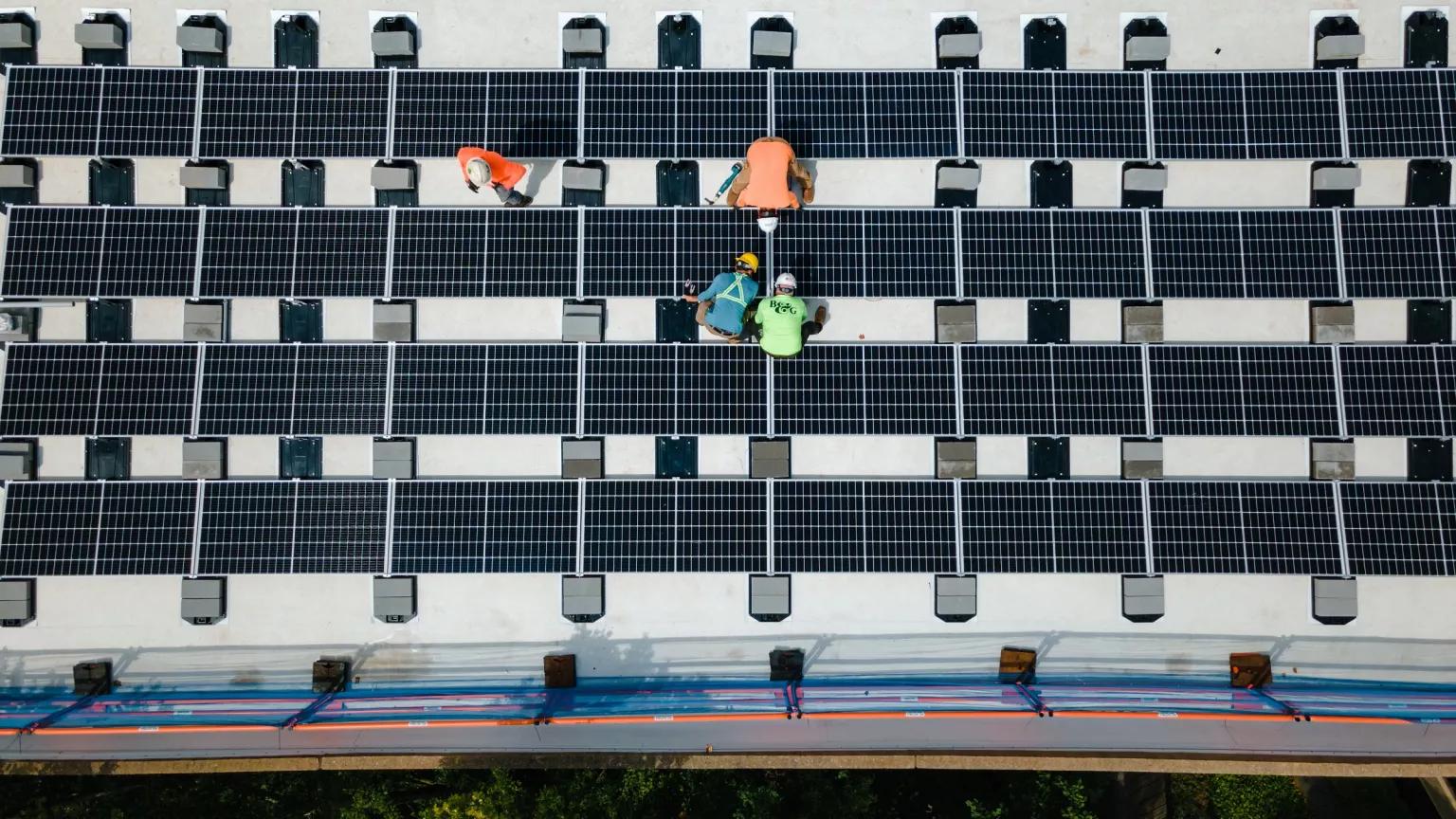 An aerial view of workers working on a solar array on a building roof