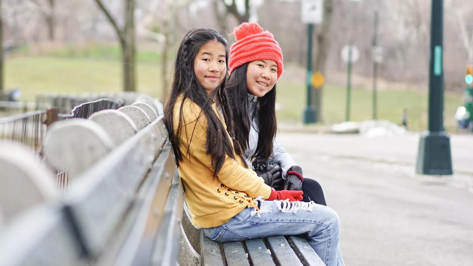 Two girls sitting on a bench in a city park