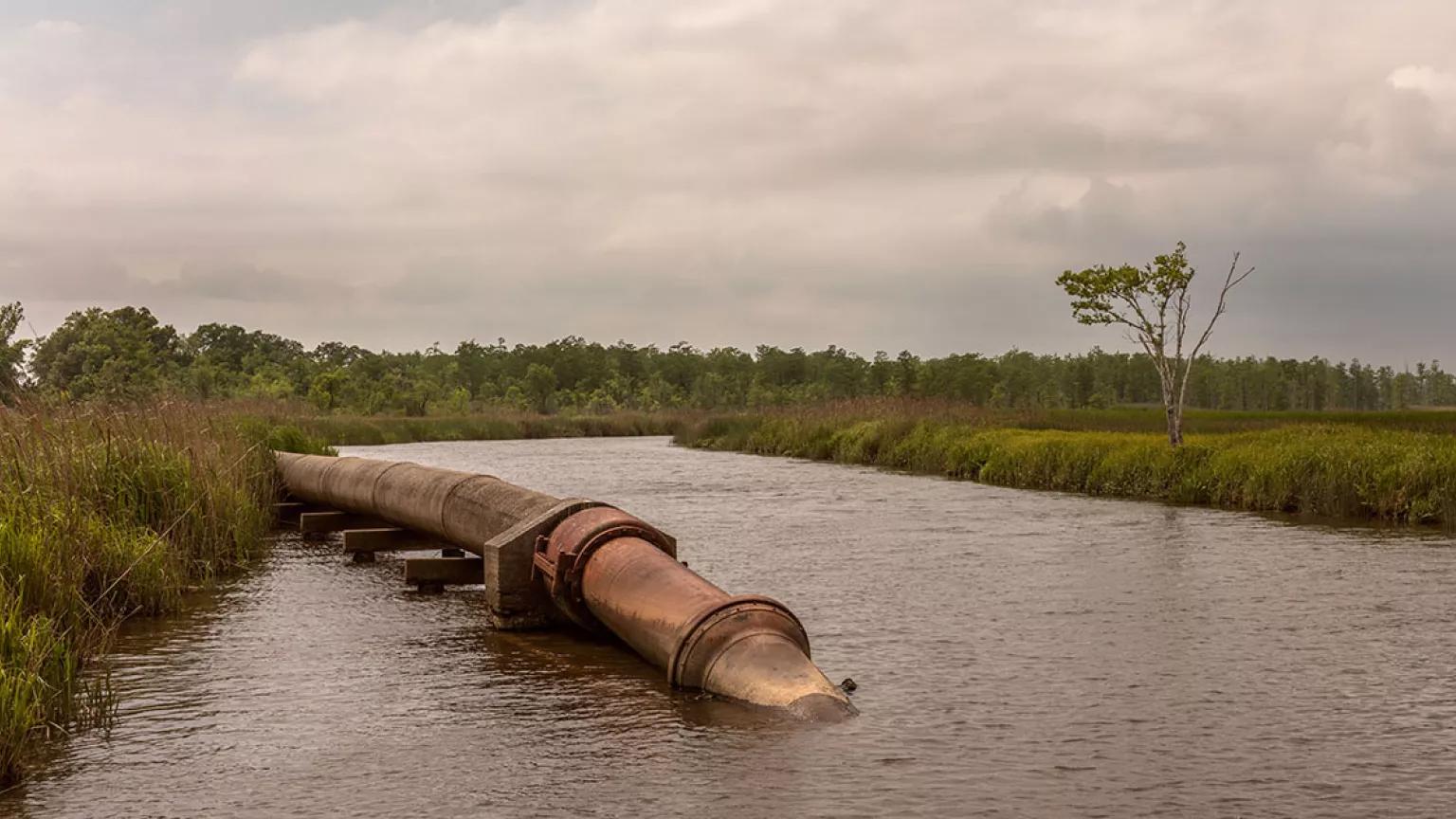 A large pipe extends from grassy land into a small river