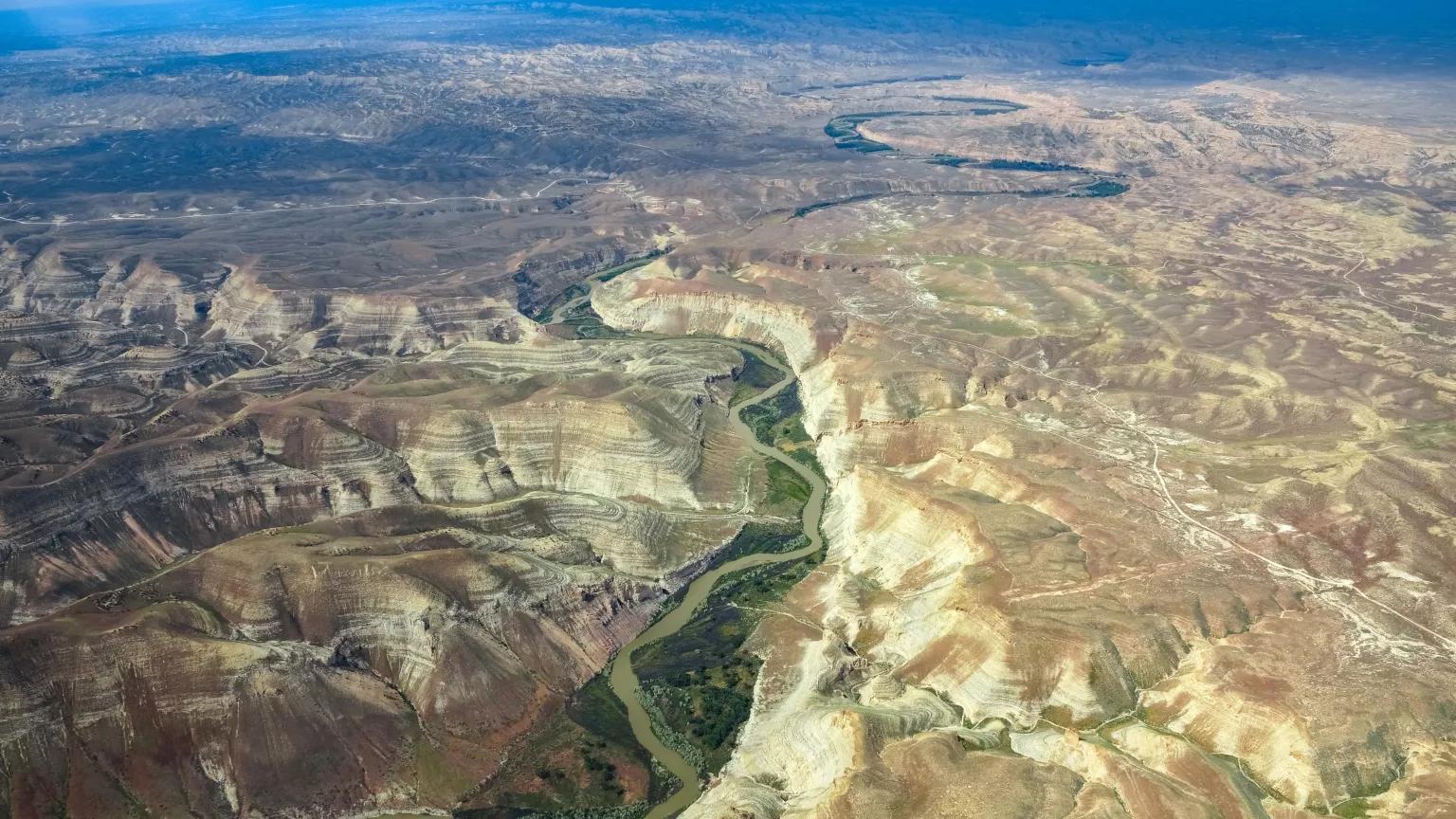 An aerial view of a green valley with a river running through it surrounded by rugged brown mountains