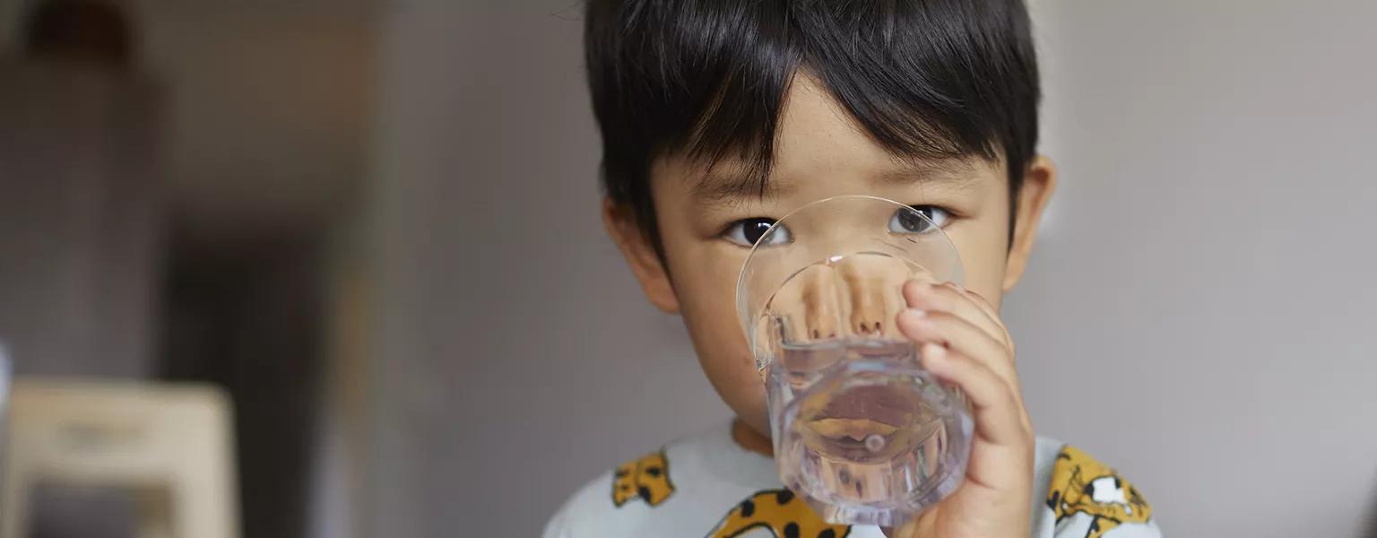 A young child facing the camera while drinking a glass of water