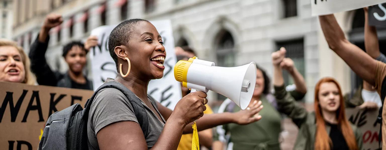 A woman speaking through a megaphone with people holding signs behind her