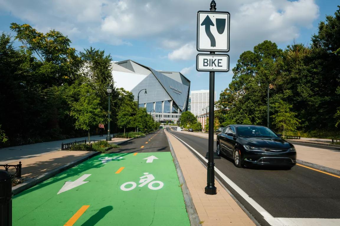 A bike lane painted green, going both ways, on Martin Luther King Jr. Drive in Atlanta, with a black car driving past and a bike lane sign