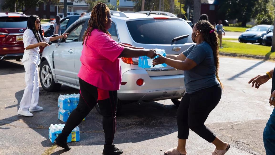 Two residents of Benton Harbor, Michigan, carry bottled water at a pickup site at the garage of the Gods Household of Faith campus