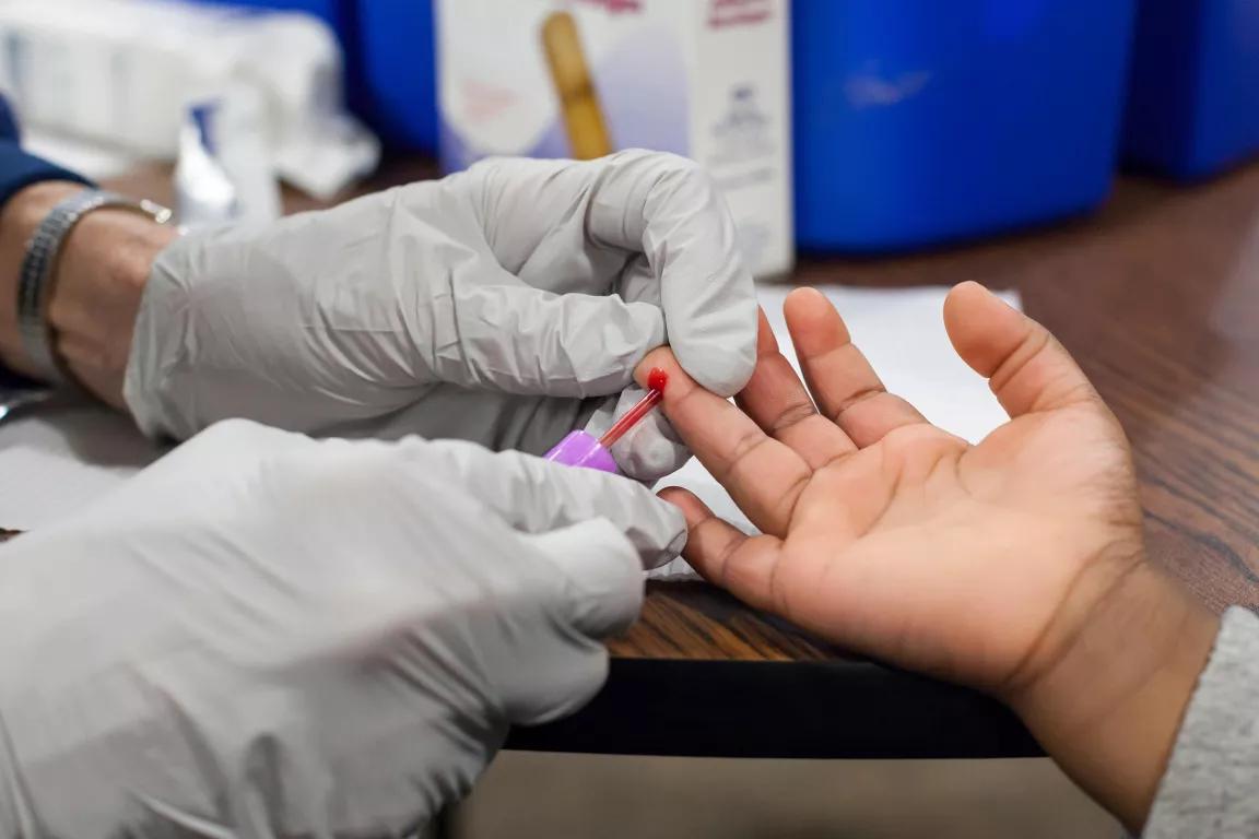 A pair of gloved hands pricking blood from a child's hand