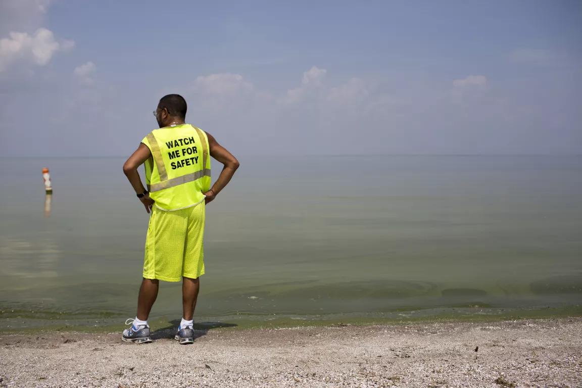 A person standing in neon yellow top and shorts, with their back to the camera. Back of the shirt says "Watch me for safety."
