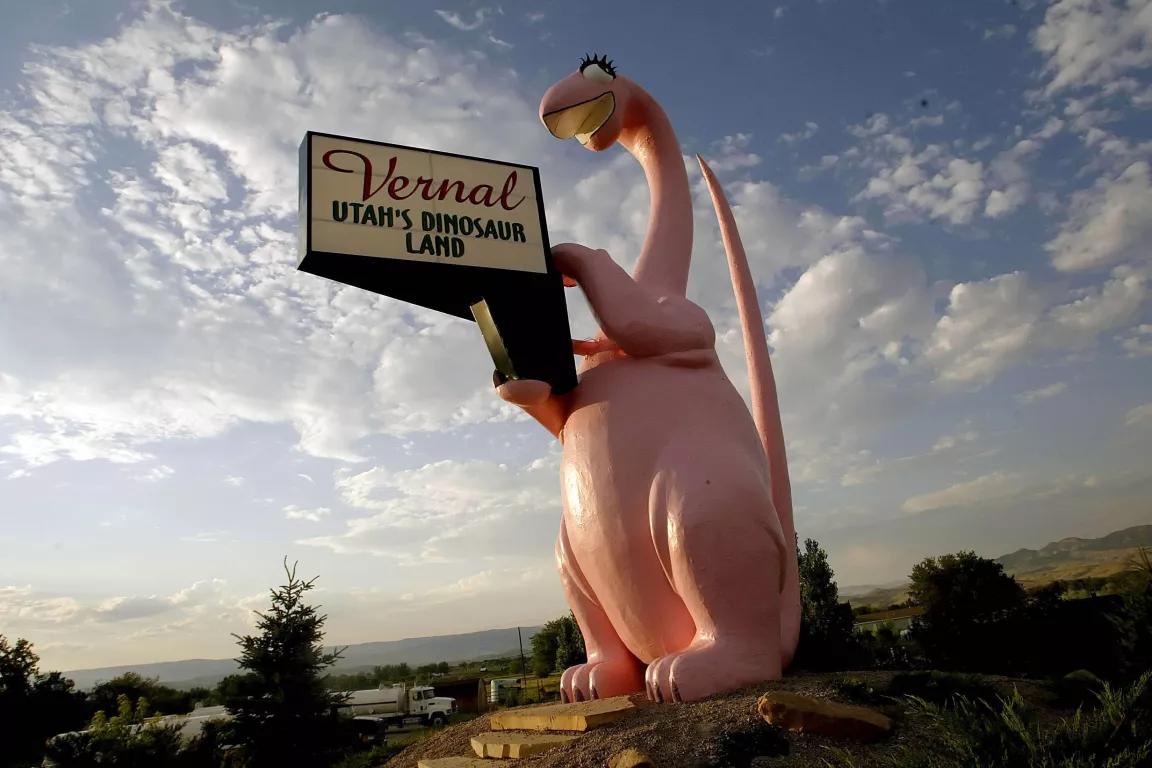 A giant statue of a pink dinosaur holds a sign that reads "Vernal, Utah's Dinoasur Land"