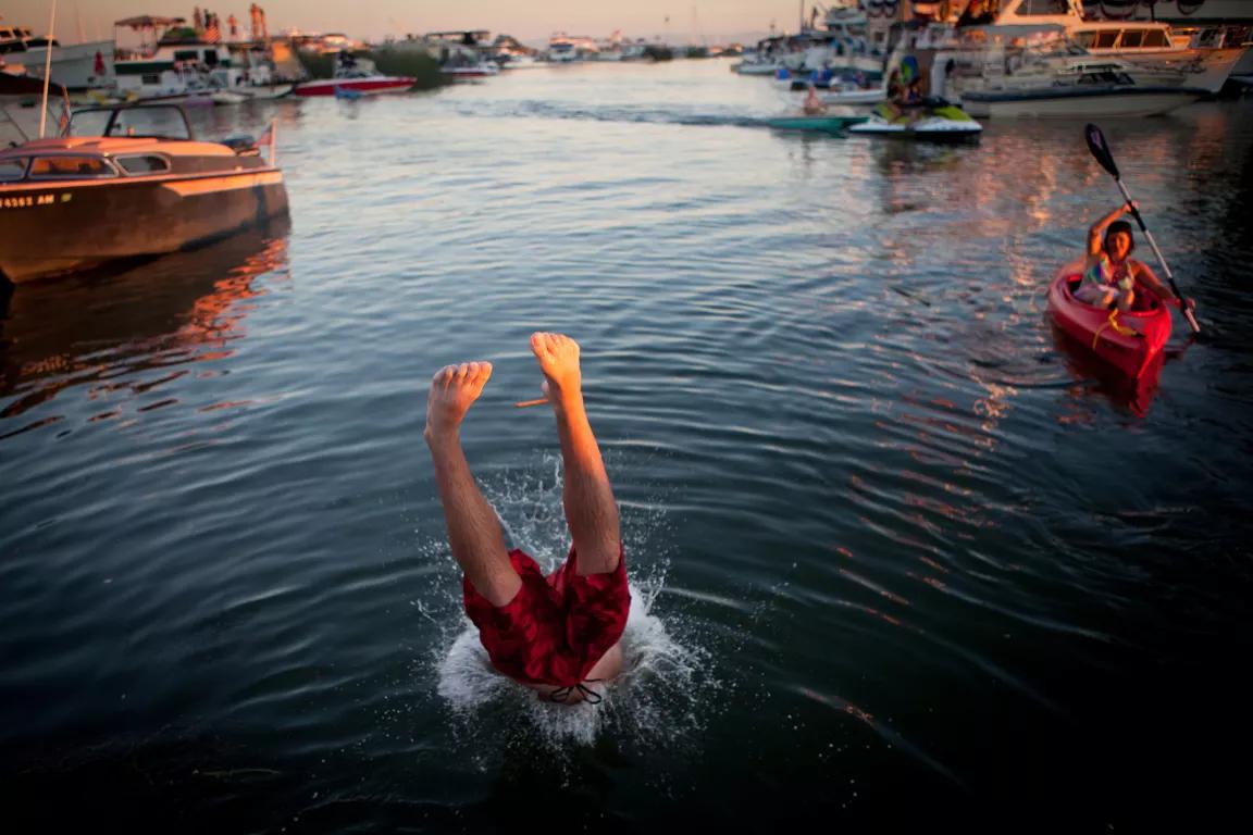 A person dives into the water near where a kayaker paddlees, with small boats nearby