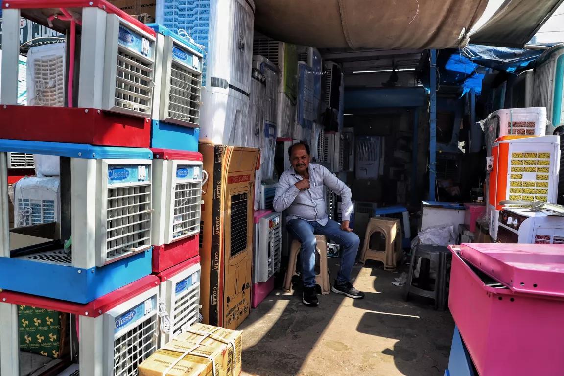 A person sits outside next to air-conditioning units stacked on top of each other