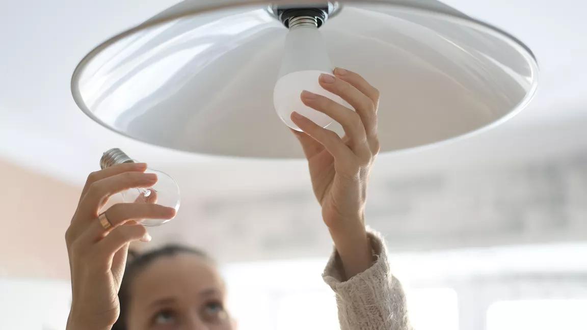 A person replaces an incandescent lightbulb with a new LED bulb.