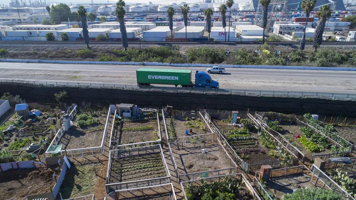 A freight truck travels on a highway with small garden plots in the foreground.