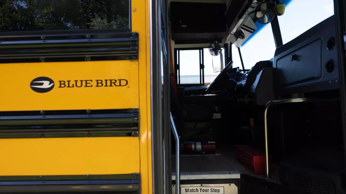 The driver's seat of a yellow school bus seen from the door of the bus