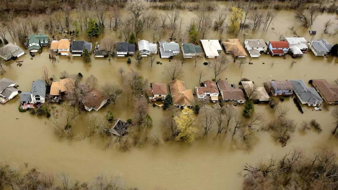 An aerial view of two rows of single-family homes that are completely surrounded by brown floodwaters.