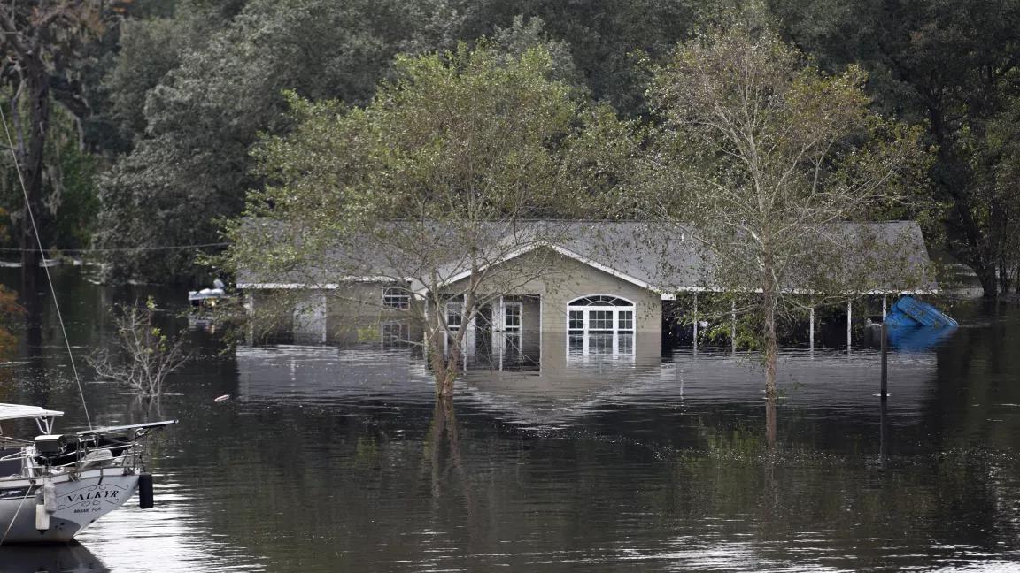 A boat floats outside of a one-story house that is flooded nearly up to its roof.