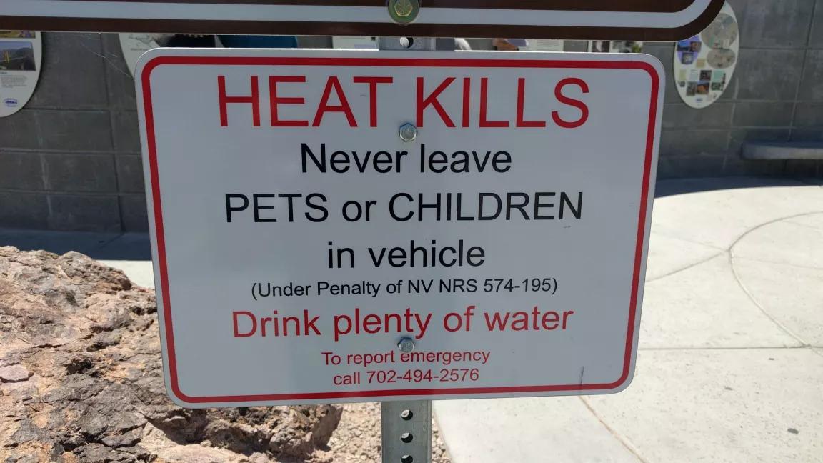 Close up on a white sign that says HEAT KILLS in big red letters. It warns people not to leave pets or kids in cars and to drink lots of water.