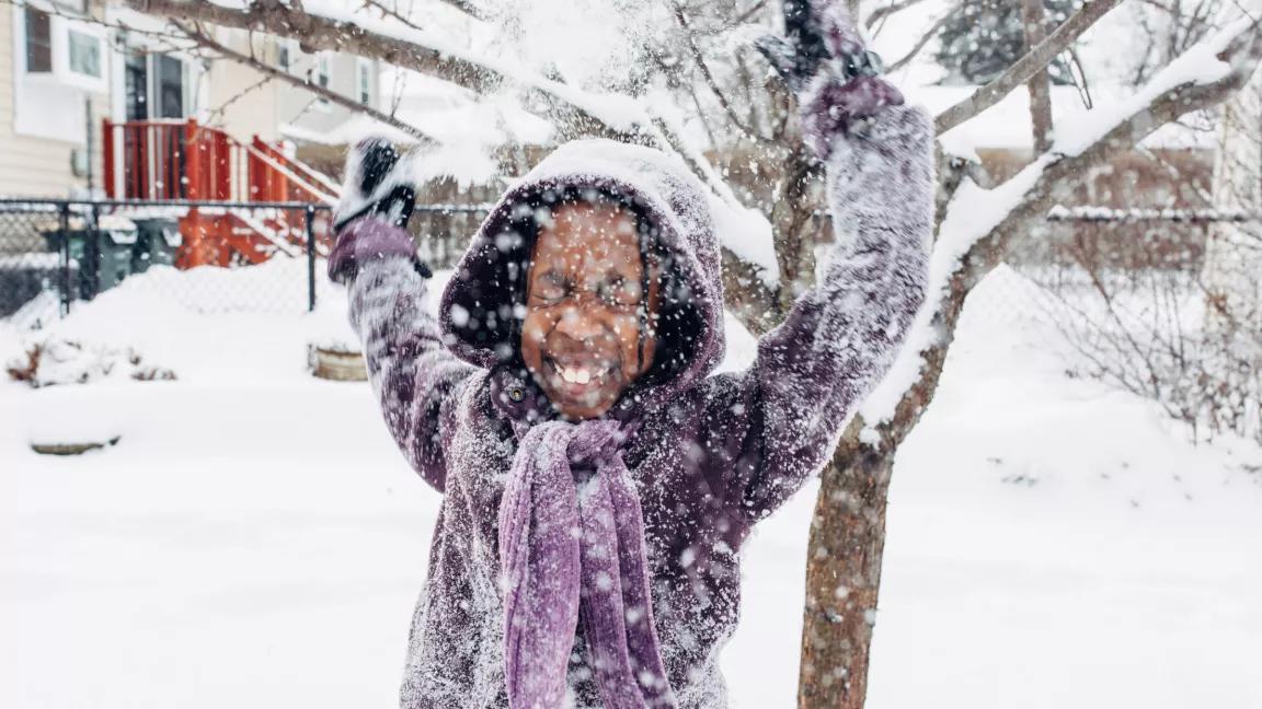 Young person playing in snowy yard with house in background