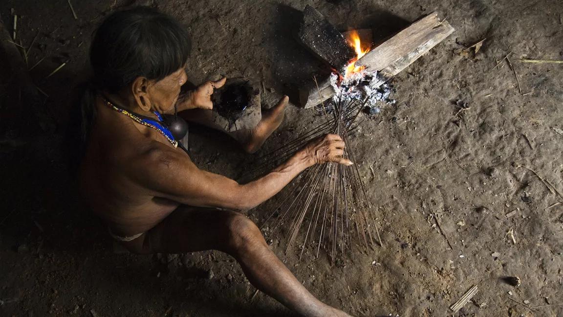 A man uses thin sticks to make a fire