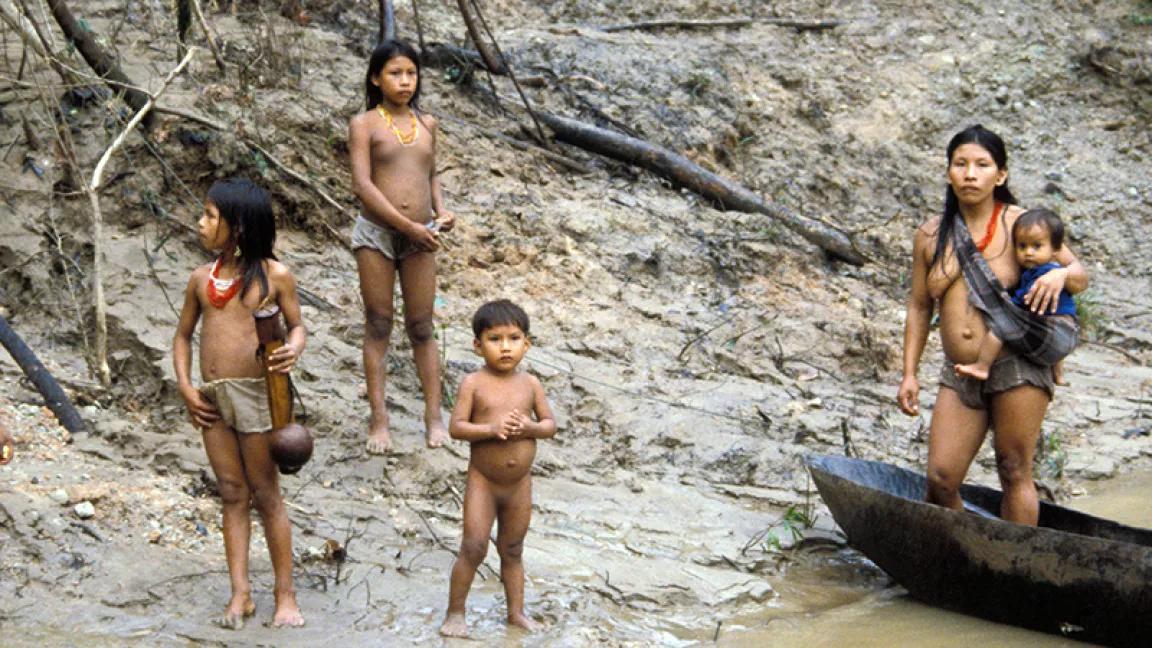 A woman and children stand on a sandy riverbank